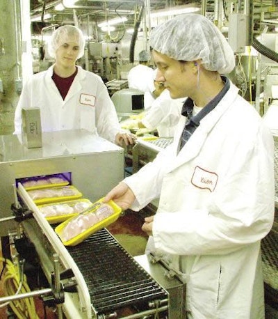 Colin Usher, research scientist and project director, feeds a tray pack package to Georgia Tech’s automatic inspection system as co-op student, Parker McGee, looks on. The system is currently undergoing a field trial at a Fieldale Farms’ processing plant. Installed beside a conveyor that handles the output of packages from several sealing machines, the system is being evaluated for its accuracy in identifying defects – such as film tears – in the seals of packages.