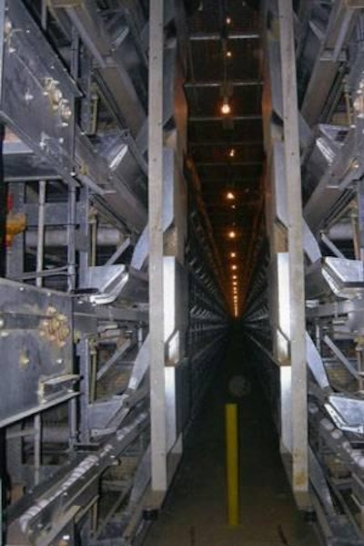 Feed cart installed on Tecno battery installation distributes feed to 12 tiers along a 400-foot cage row. Unit can be pre-programmed as to the desired number of feedings per day. Bottom six tiers are shown with a catwalk above and lights suspended at staggered heights for optimal illumination.