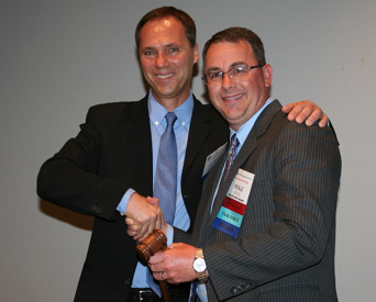 Outgoing USAPEEC Chairman Charles von der Heyde of Pilgrim&rsquo;s Mexico, left, passes the ceremonial Hoben Gavel to Mike Little of Mountaire Farms, who assumes the chairmanship for 2014-15. The gavel is named for two-time USAPEEC Chairman Jim Hoben, who crafted the piece in his wood shop.