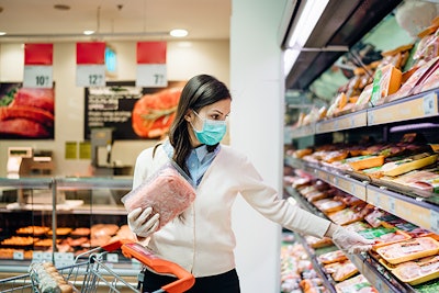 Shopper with mask safely buying for groceries due to coronavirus pandemic in grocery store.COVID-19 shopping for meat and animal products.Quarantine preparation.Panic buying and stockpiling.