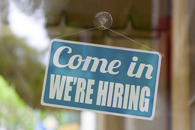 Close-up on a blue sign in the window of a shop displaying the message: Come in we 're hiring.