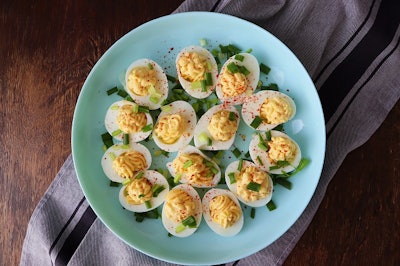 Deviled Eggs sprinkled with paprika and chopped green onion on a green plate on a woodene table . Top view .