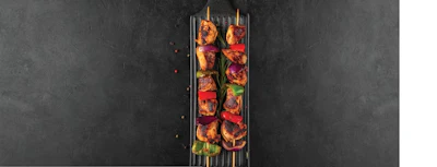 Grilled meat and vegetable kebabs on skewers over a charcoal grill with fresh herbs